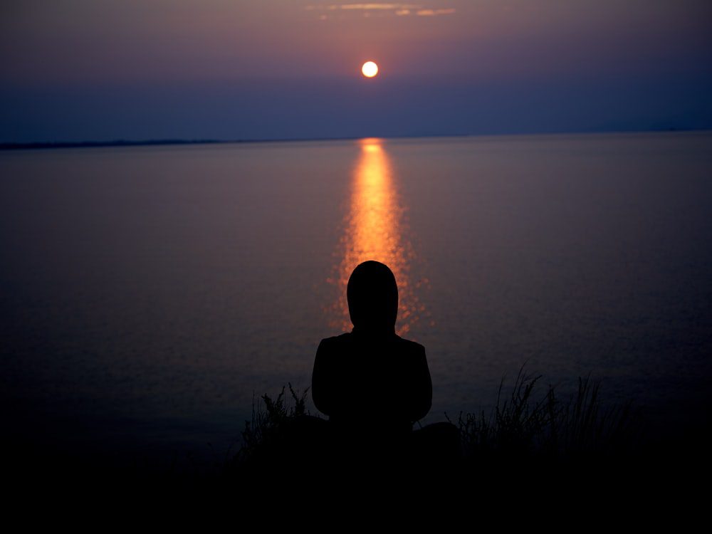 Silhouette of a person sitting on grass at sunset, grounded and calm in the therapeutic process