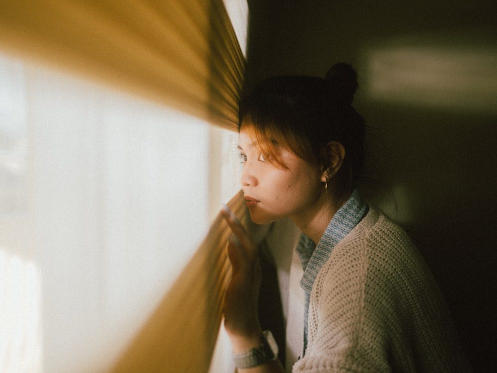 Woman looking out a window in soft light, reflecting on her inner world in psychodynamic therapy
