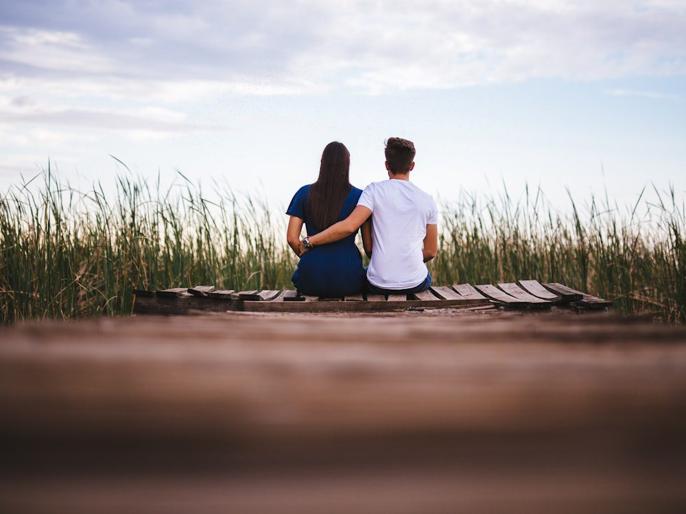 Two partners sitting side by side on a wooden dock in soft light, supported together in couples therapy
