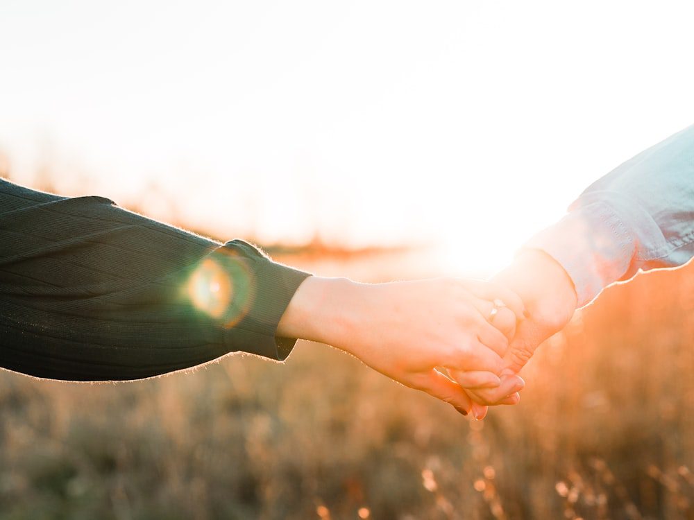Two people reaching toward each other and holding hands at sunset, a corrective emotional experience in couples therapy