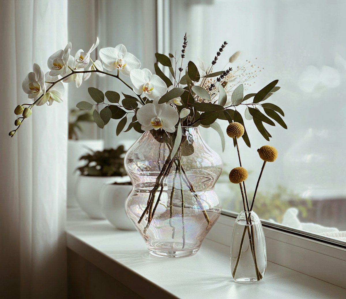 Orchids and dried flowers in a glass vase on a bright windowsill, representing EMDR therapy