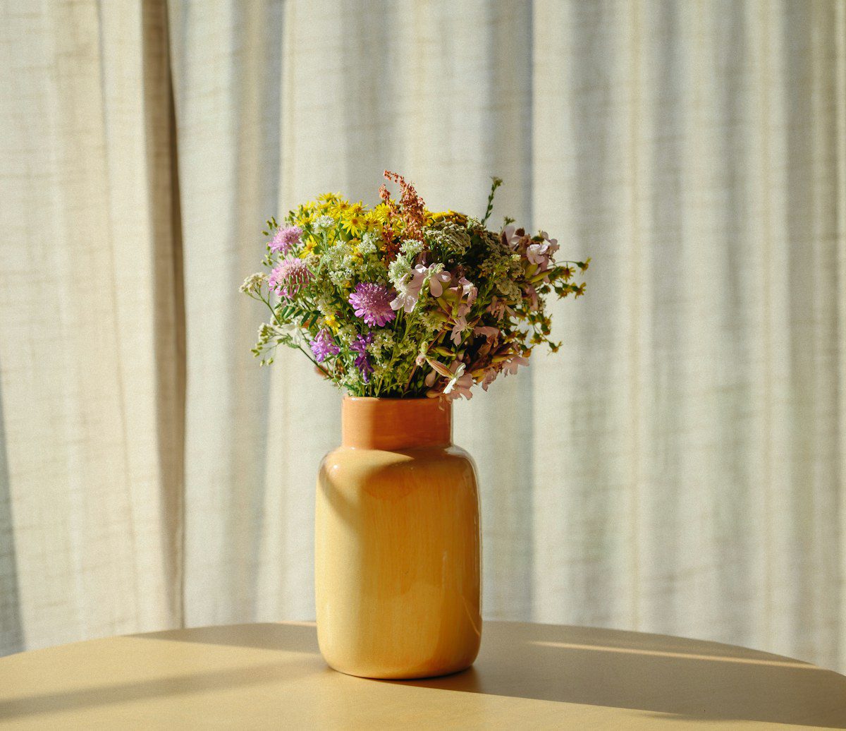 Wildflowers in a yellow ceramic vase by a sheer curtain, representing experiential therapy