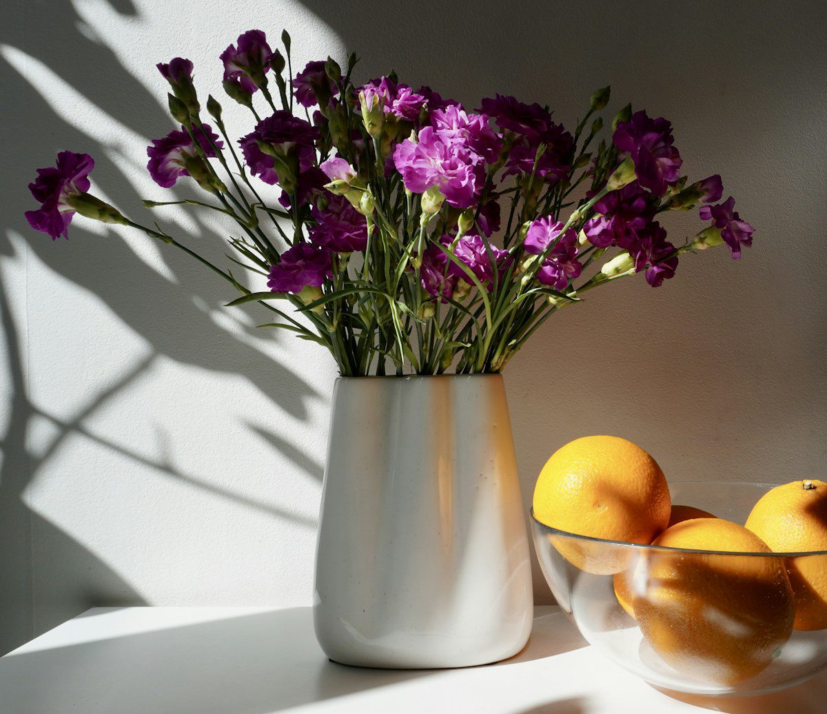 Purple carnations in a white vase beside a bowl of oranges, representing psychodynamic therapy