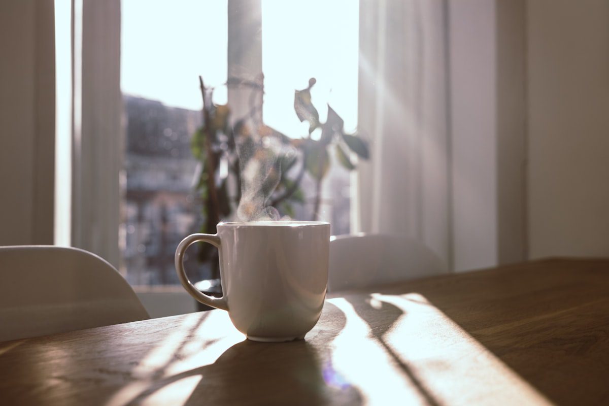 A steaming mug on a wooden table by a sunlit window