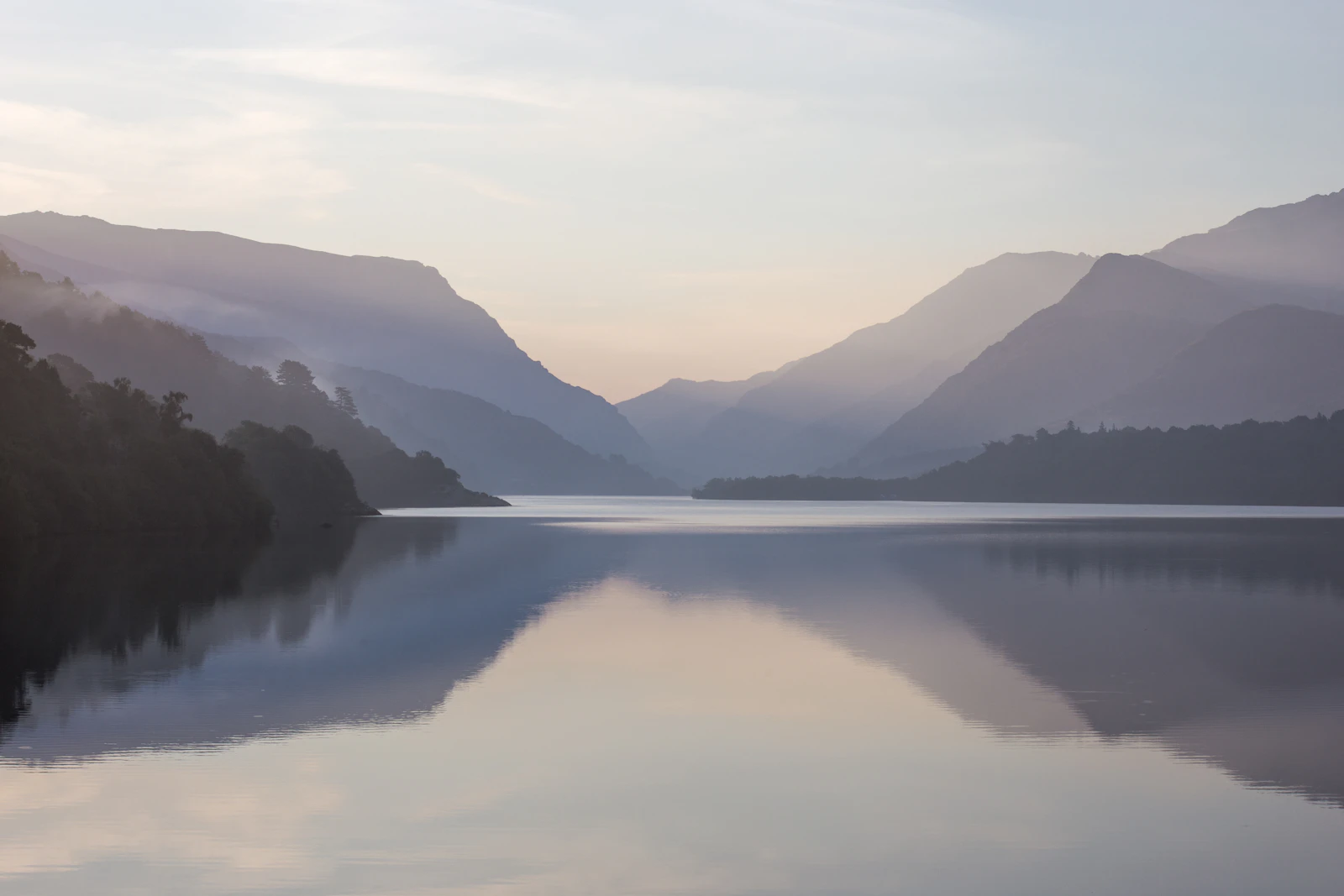 A calm lake reflecting soft mountains in morning light