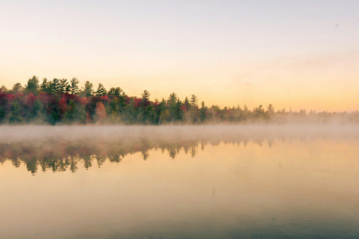 Morning mist lifting over a calm lake lined with autumn trees